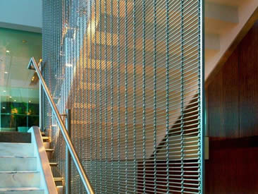 A corner of stairs and beside the stair is green architectural cable mesh.